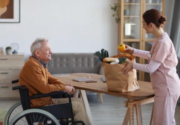 a senior sitting in a wheelchair while an attendant unloads groceries