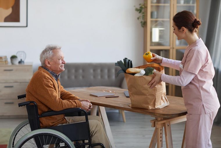 a senior sitting in a wheelchair while an attendant unloads groceries