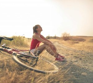 a woman sitting beside her bike in the sun smiling