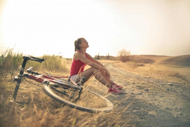 a woman sitting beside her bike in the sun smiling