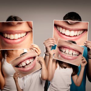 young family with children holding a picture of a mouth smiling on a gray background