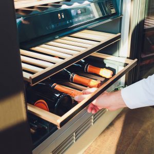 a man pulling out the drawer on a wine cooler