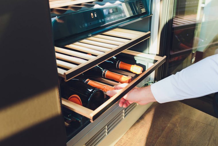 a man pulling out the drawer on a wine cooler