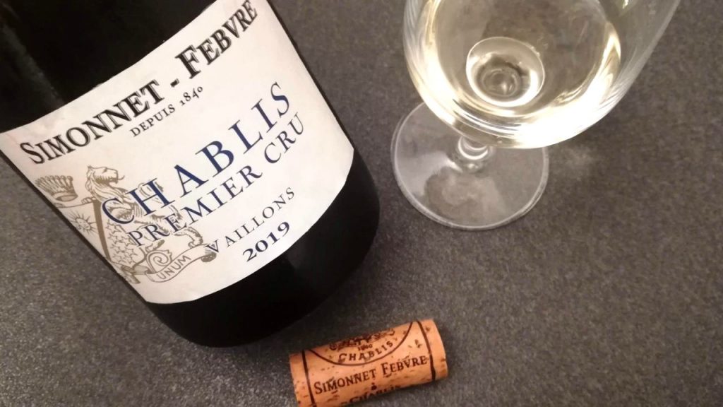 a bottle of chablis with a full wine glass and a cork on the table