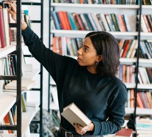a woman picking paper books off a shelf