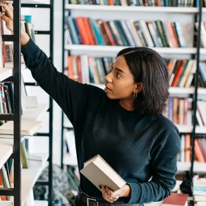 a woman picking paper books off a shelf