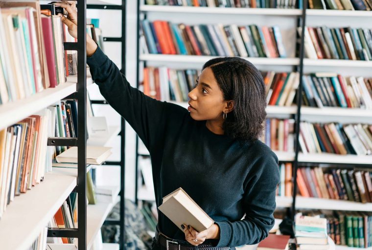 a woman picking paper books off a shelf