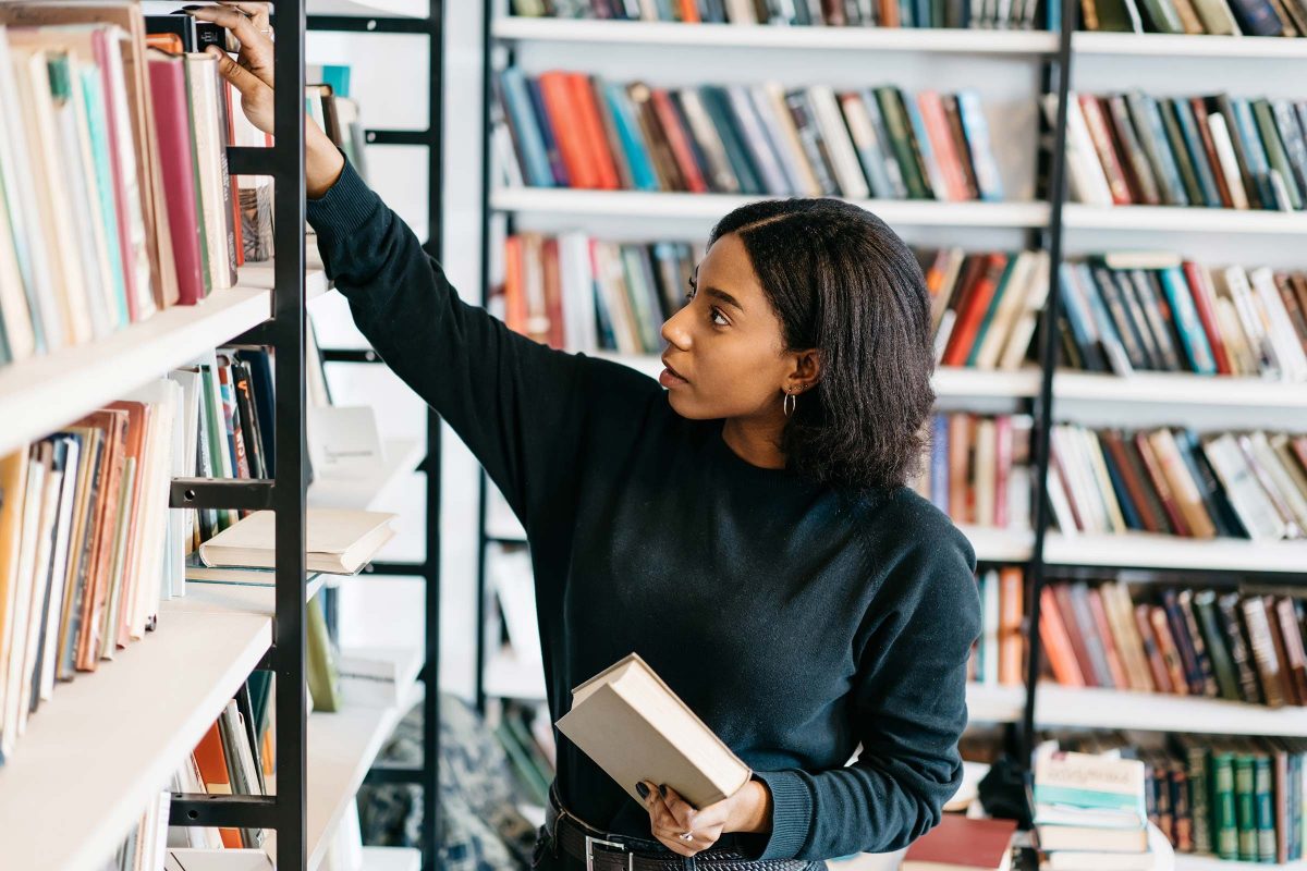 a woman picking paper books off a shelf