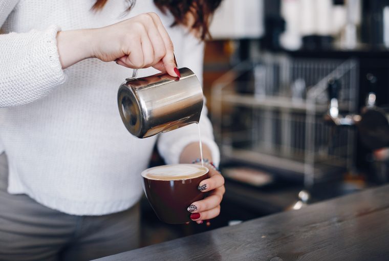 A girl pours milk foam into coffee. Waitress prepares coffee. Woman is pouring milk into coffee cup