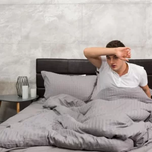 a man wiping his forehead in bed
