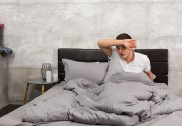 a man wiping his forehead in bed