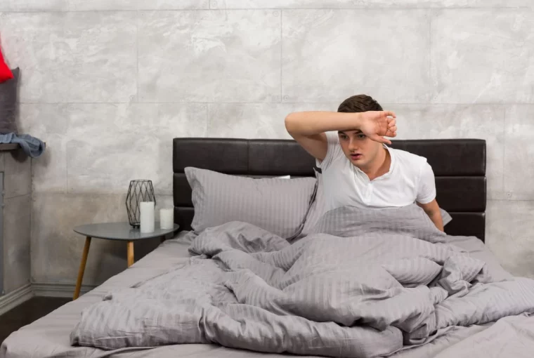 a man wiping his forehead in bed