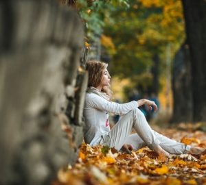 a woman sitting outside in the fall under a tree