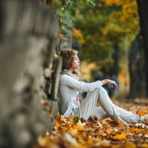 a woman sitting outside in the fall under a tree